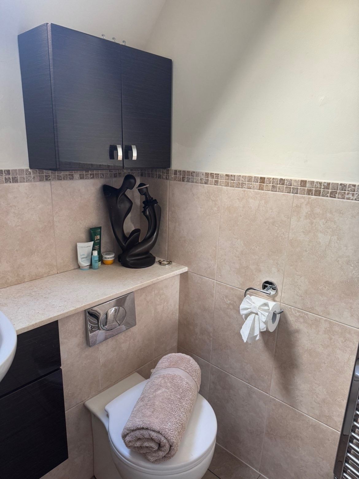 Bathroom with a towel neatly rolled on the cistern and a folded paper bow on the holder