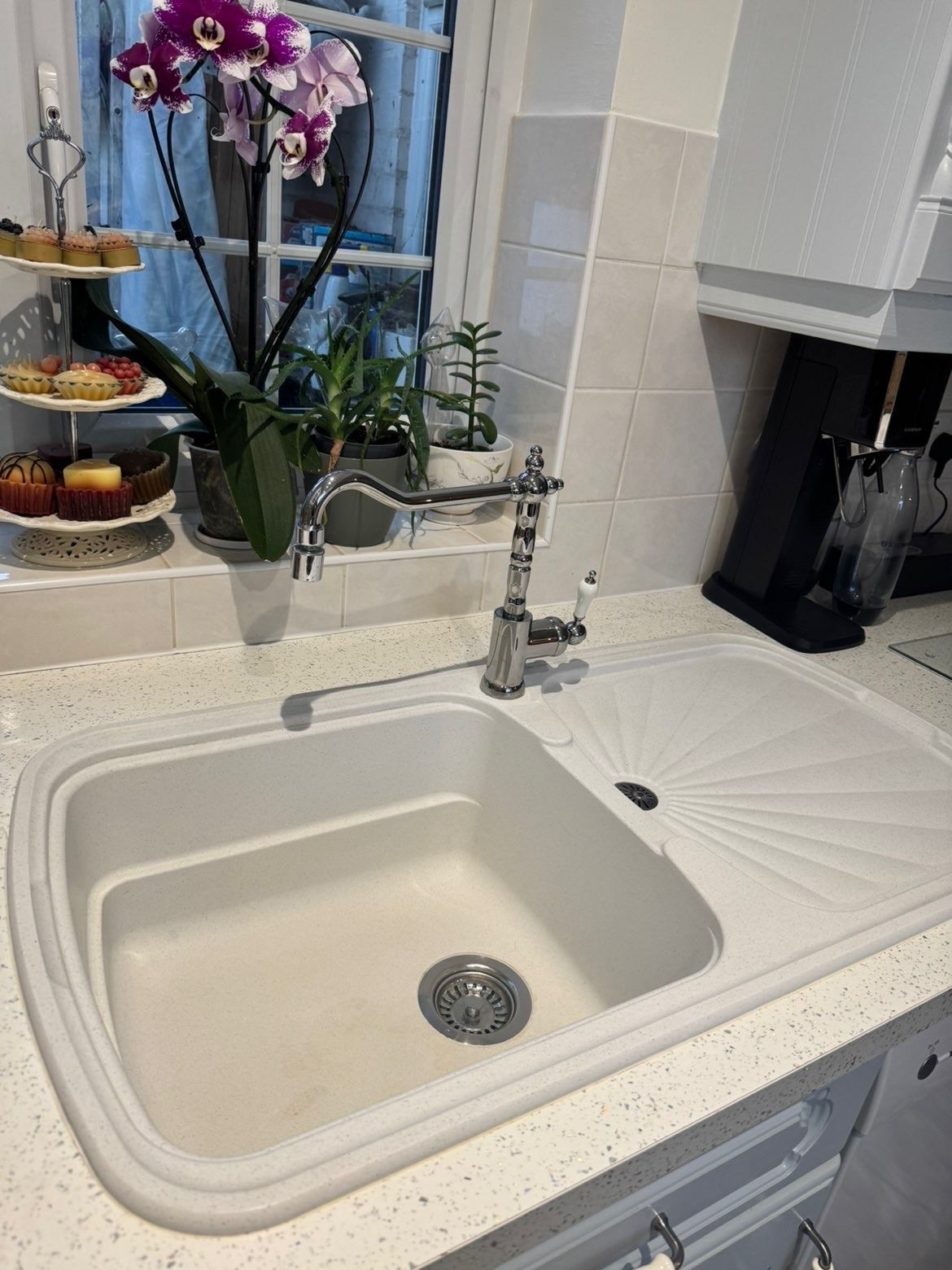 Polished cream kitchen sink and chrome tap with an orchid on the windowsill